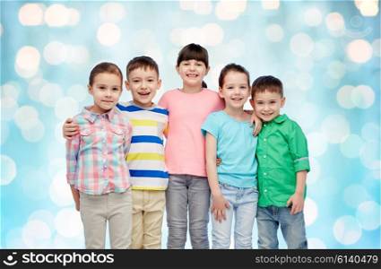childhood, fashion, friendship and people concept - group of happy smiling little children hugging over blue holidays lights background