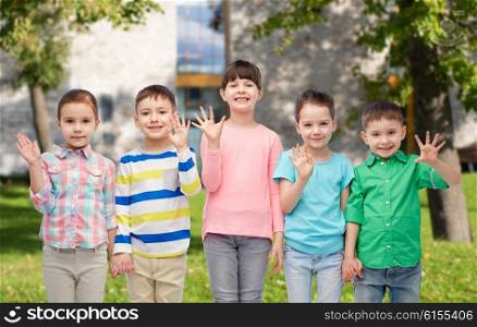 childhood, fashion, friendship and people concept - group of happy smiling little children holding hands over summer campus background