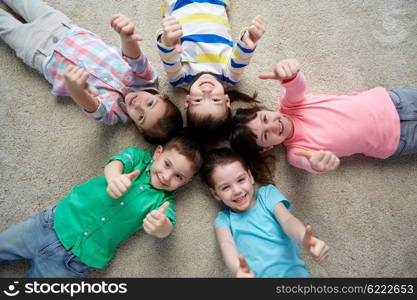 childhood, fashion, friendship and people concept - group of happy smiling little children lying on floor and showing thumbs up