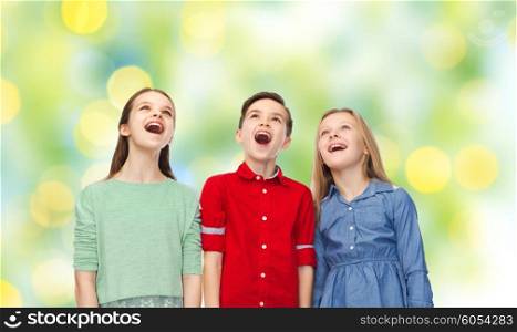 childhood, fashion, friendship and people concept - happy amazed boy and girls looking up with open mouths over green lights background