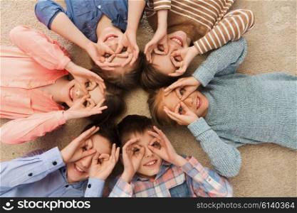 childhood, fashion, friendship and people concept - happy children lying in circle on floor, making faces and having fun