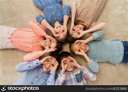 childhood, fashion, friendship and people concept - happy children lying in circle on floor, making faces and having fun