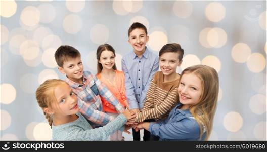 childhood, fashion, friendship and people concept - happy children with hands on top over holidays lights background