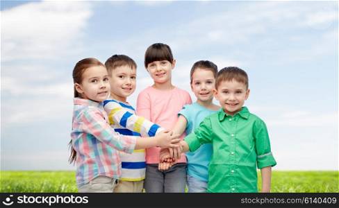 childhood, fashion, friendship and people concept - happy little children with hands on top over blue sky and grass background