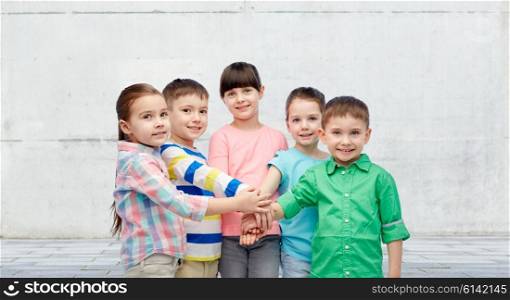 childhood, fashion, friendship and people concept - happy little children with hands on top over concrete wall on street background