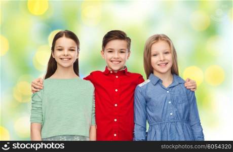 childhood, fashion, friendship and people concept - happy smiling boy and girls hugging over green lights background