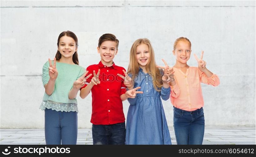 childhood, fashion, friendship and people concept - happy smiling boy and girls showing peace hand sign over urban street background