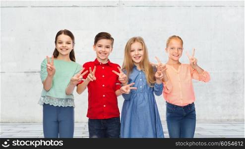 childhood, fashion, friendship and people concept - happy smiling boy and girls showing peace hand sign over urban street background