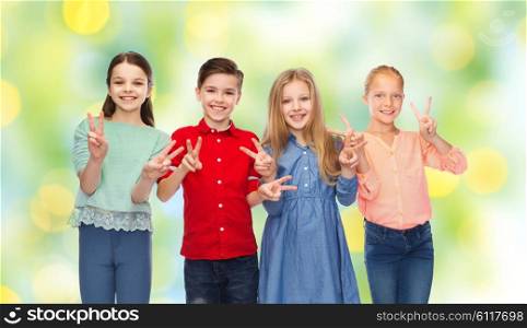 childhood, fashion, friendship and people concept - happy smiling boy and girls showing peace hand sign over green summer holidays lights background