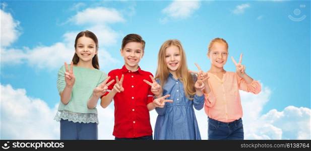 childhood, fashion, friendship and people concept - happy smiling boy and girls showing peace hand sign over blue sky and clouds background