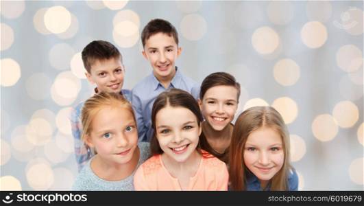childhood, fashion, friendship and people concept - happy smiling children faces over holidays lights background