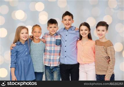 childhood, fashion, friendship and people concept - happy smiling children hugging over holidays lights background