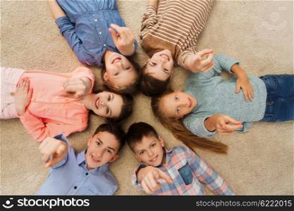 childhood, fashion, friendship and people concept - happy smiling children pointing finger to you and lying on floor in circle