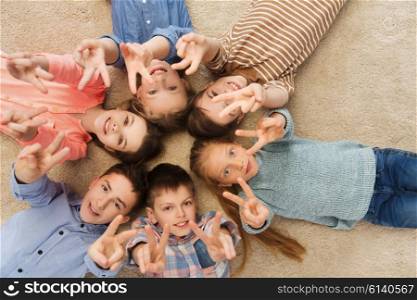 childhood, fashion, friendship and people concept - happy smiling children showing peace hand sign and lying on floorin circle