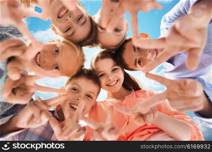 childhood, fashion, friendship and people concept - happy smiling children showing peace hand sign and standing in circle over blue sky and clouds background