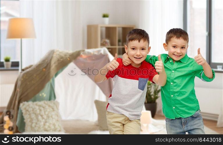 childhood, fashion, friendship and people concept - happy smiling little boys showing thumbs up over kids room and tepee background. happy smiling little boys showing thumbs up
