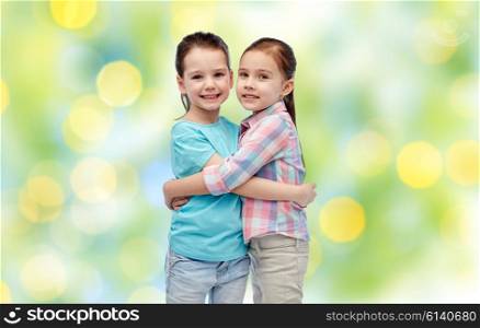 childhood, fashion, friendship and people concept - happy smiling little girls hugging over summer green lights background