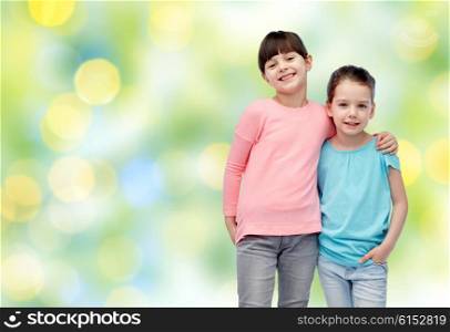 childhood, fashion, friendship and people concept - happy smiling little girls hugging over summer green lights background