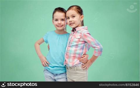 childhood, fashion, friendship and people concept - happy smiling little girls hugging over green school chalk board background