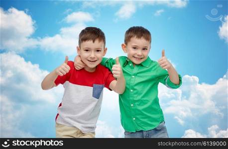 childhood, fashion, friendship, gesture and people concept - happy smiling little boys showing thumbs up over blue sky and clouds background
