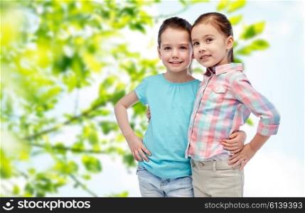 childhood, fashion, friendship, summer and people concept - happy smiling little girls hugging over green natural background