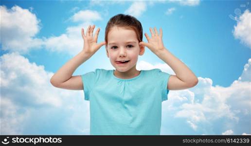 childhood, fashion, fun and people concept - happy little girl having fun and making ears over blue sky and clouds background