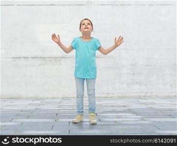 childhood, fashion, fun and people concept - happy little girl looking up to something over urban concrete background