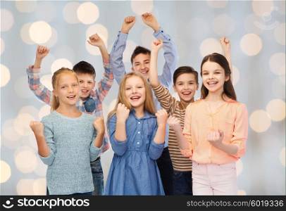 childhood, fashion, gesture and people concept - happy children friends raising fists and celebrating victory over holidays lights background