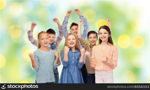 childhood, fashion, gesture and people concept - happy children friends raising fists and celebrating victory over green lights background