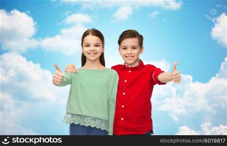 childhood, fashion, gesture and people concept - happy smiling boy and girl hugging and showing thumbs up over blue sky and clouds background