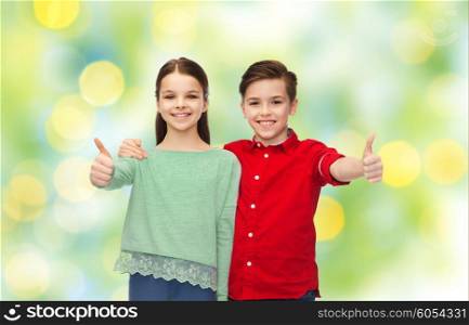 childhood, fashion, gesture and people concept - happy smiling boy and girl hugging and showing thumbs up over green lights background