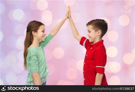 childhood, fashion, gesture and people concept - happy smiling boy and girl making high five over pink holidays lights background