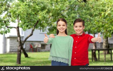 childhood, fashion, gesture and people concept - happy smiling boy and girl hugging and showing thumbs up over private house backyard background