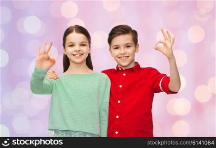 childhood, fashion, gesture and people concept - happy smiling boy and girl hugging and showing ok hand sign over pink holidays lights background