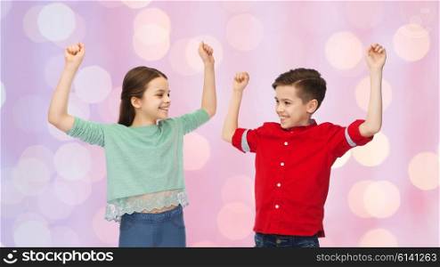 childhood, fashion, gesture and people concept - happy smiling boy and girl raising fists and celebrating victory over pink holidays lights background