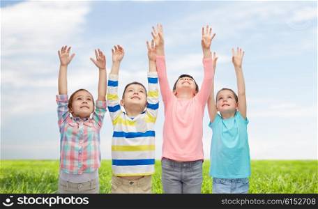 childhood, fashion, gesture and people concept - happy smiling children raising hands and celebrating victory over blue sky and grass background
