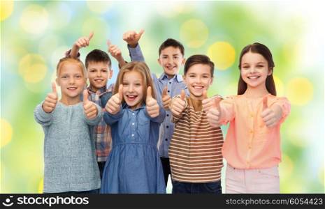 childhood, fashion, gesture and people concept - happy smiling children showing thumbs up over green lights background