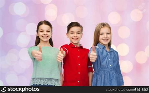 childhood, fashion, gesture and people concept - happy smiling children showing thumbs up over pink holidays lights background