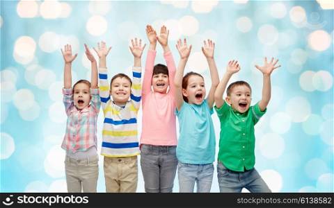 childhood, fashion, gesture and people concept - happy smiling friends raising fists and celebrating victory over blue holidays lights background
