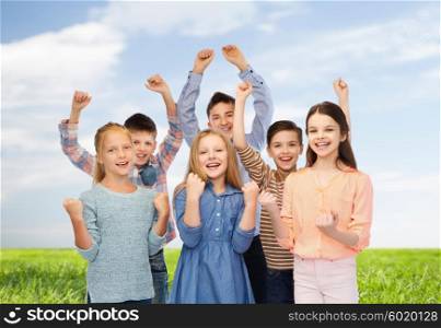 childhood, fashion, gesture, summer and people concept - happy children friends raising fists and celebrating victory over blue sky and grass background