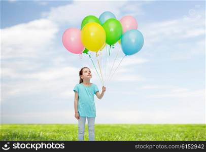 childhood, fashion, imagination and people concept - happy little girl looking up and holding bunch of colorful helium balloons on strand over blue sky and grass background