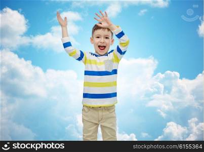 childhood, fashion, joy and people concept - happy little boy waving hands over blue sky and clouds background