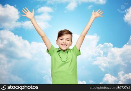 childhood, fashion, power, joy and people concept - happy smiling boy in green polo t-shirt raising hands up over blue sky and clouds background