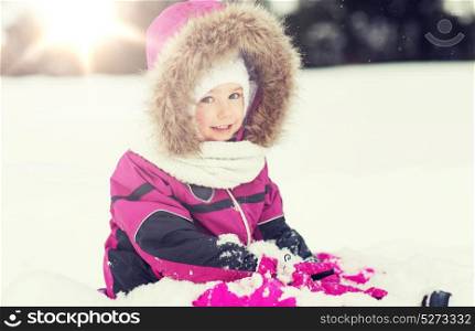 childhood, fashion, season and people concept - happy little kid in winter clothes playing with snow outdoors. happy kid in winter clothes playing with snow
