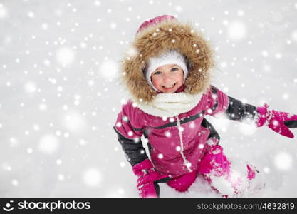 childhood, fashion, season and people concept - happy little kid or girl in winter clothes playing with snow