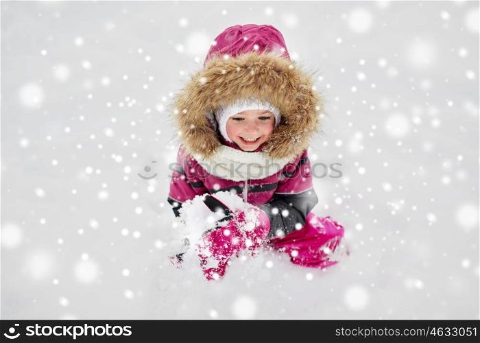 childhood, fashion, season and people concept - happy little kid or girl in winter clothes playing with snow
