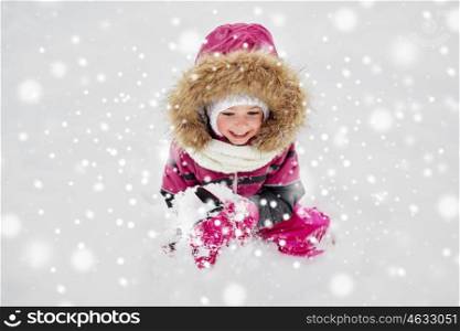 childhood, fashion, season and people concept - happy little kid or girl in winter clothes playing with snow