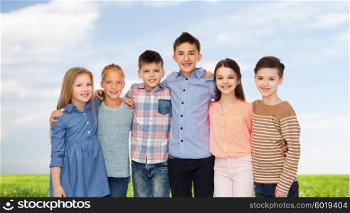 childhood, fashion, summer, friendship and people concept - happy smiling children hugging over blue sky and grass background