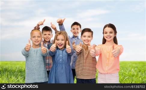 childhood, fashion, summer, gesture and people concept - happy smiling children showing thumbs up over blue sky and grass background