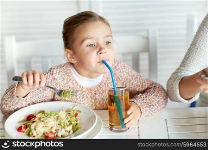childhood, food and people concept - little girl eating pasta and drinking apple juice for dinner at restaurant or cafe